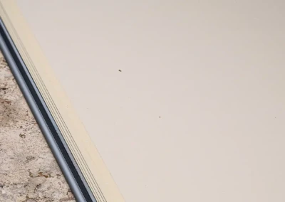 Chez-Camille-et-Arthur-4 Joint en métal gris séparant un sol en pierre beige d'une surface blanche lisse.