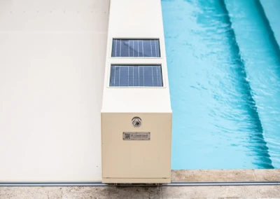 Chez-Camille-et-Arthur-6 Boîtier blanc avec panneaux solaires à côté d'une piscine bleue, sur un sol en pierre beige.
