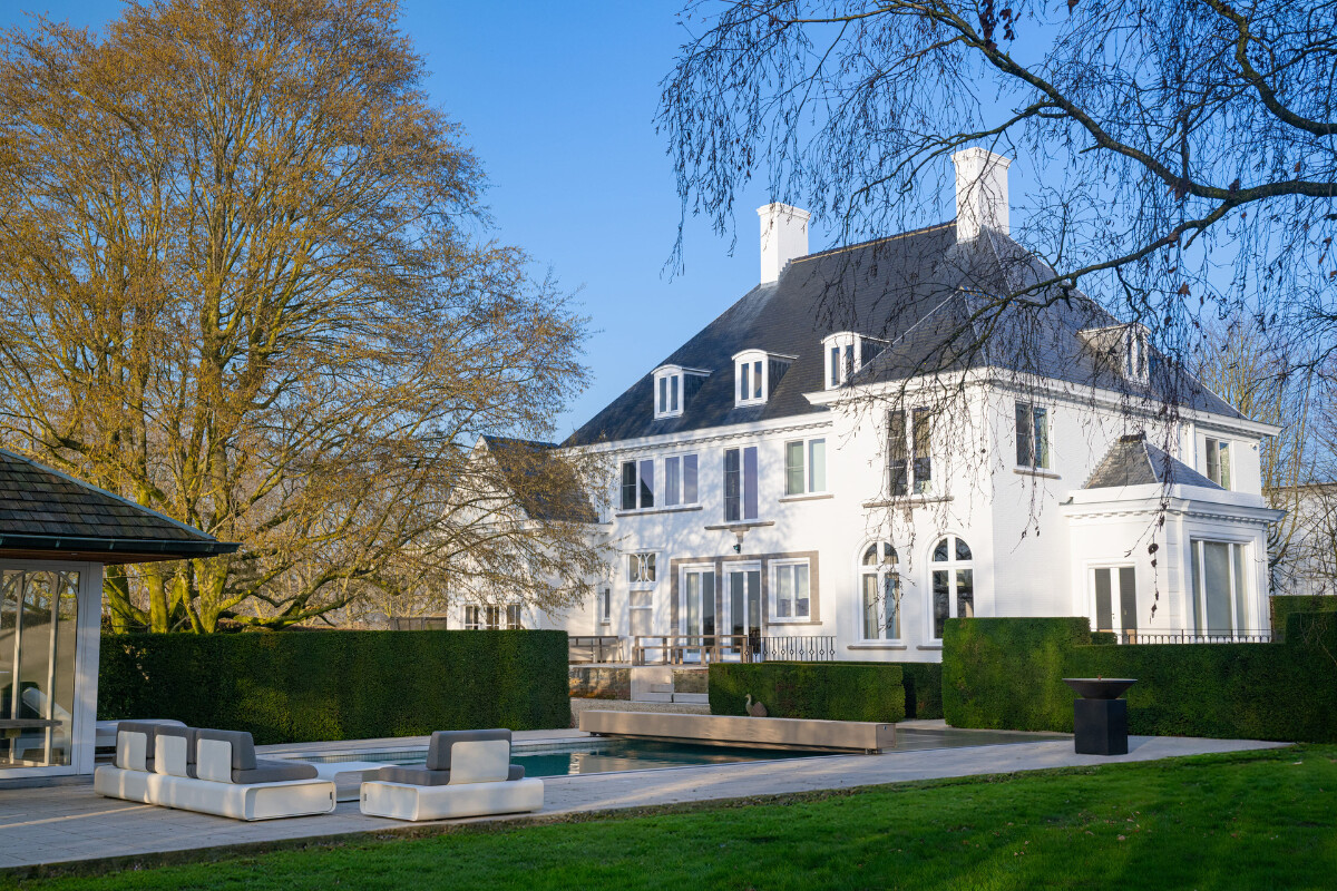 Een metalen kast met een label, omringd door stenen, staat naast een zwembad met helderblauw water en gras.